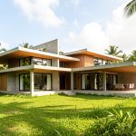 Maison contemporaine antillaise en construction sur un terrain verdoyant, entourée de végétation tropicale sous un ciel lumineux.