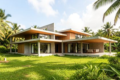 Maison contemporaine antillaise en construction sur un terrain verdoyant, entourée de végétation tropicale sous un ciel lumineux.