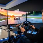 Un homme concentré conduit un simulateur automobile équipé d’un cockpit, d’un volant de course et de trois écrans dans un centre de loisirs moderne.