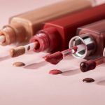 Plusieurs rouges à lèvres liquides mats ouverts avec leurs applicateurs visibles, dans des teintes nude, rouge et prune, sur un fond rose poudré éclairé par une lumière douce.