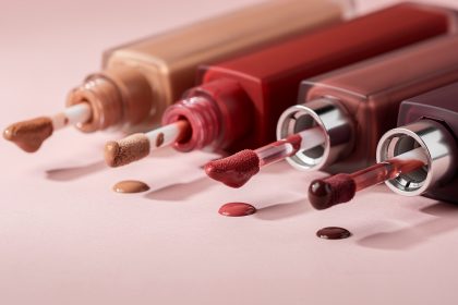 Plusieurs rouges à lèvres liquides mats ouverts avec leurs applicateurs visibles, dans des teintes nude, rouge et prune, sur un fond rose poudré éclairé par une lumière douce.
