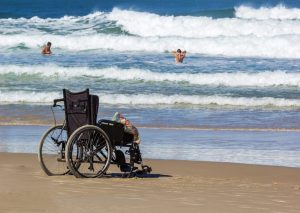 Personne en fauteuil roulant avançant sur un tapis d’accès vers une plage des Antilles.
