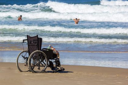 Personne en fauteuil roulant avançant sur un tapis d’accès vers une plage des Antilles.