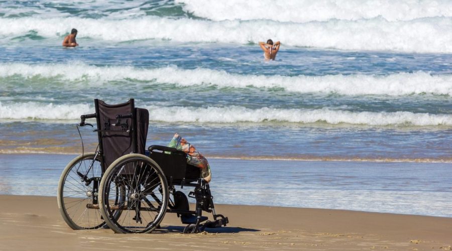 Personne en fauteuil roulant avançant sur un tapis d’accès vers une plage des Antilles.