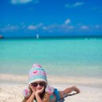 Bébé de 10 mois assis sur une plage des Caraïbes avec ses parents.