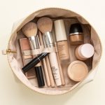 Trousse de maquillage ouverte contenant des pinceaux, une palette de fards, du mascara et plusieurs produits pour le teint sur un fond clair.