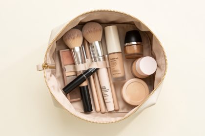 Trousse de maquillage ouverte contenant des pinceaux, une palette de fards, du mascara et plusieurs produits pour le teint sur un fond clair.