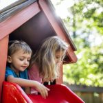 Des enfants jouent dans une cabane de jardin colorée, adaptée à leur âge et installée en extérieur.