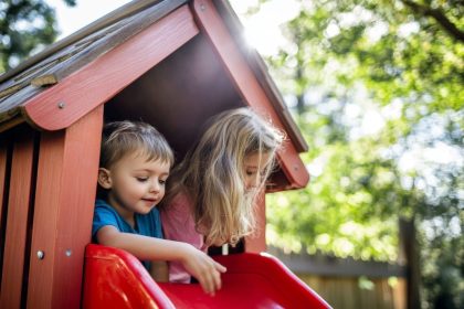 Des enfants jouent dans une cabane de jardin colorée, adaptée à leur âge et installée en extérieur.