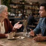 Une femme âgée et un jeune homme de générations différentes discutent chaleureusement autour d’une table dans un café réaliste.